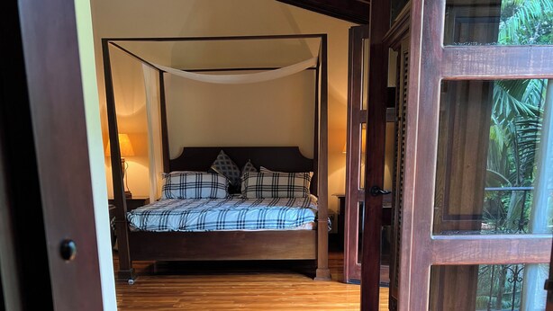 Un dormitorio con cama con dosel, suelo de madera y vistas a través de un ventanal.