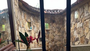 Un baño con pared de piedra, un lavabo, un espejo y una puerta que da a un espacio exterior.
