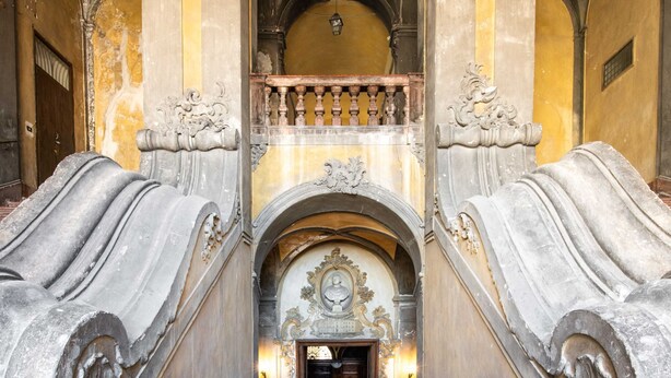 Eine prachtvolle Treppe mit aufwendigen Schnitzereien und einer Balustrade, die zu einer Tür mit dekorierter Decke führt.