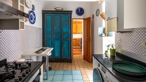 Eine Küche mit Herd, Spüle und Schränken. Ein Holztür und ein Fenster sind vorhanden.