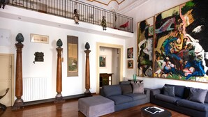 Ein geräumiges Wohnzimmer mit hoher Decke, Holzboden, einem grauen Sofa, einem Couchtisch und einem großen abstrakten Gemälde.