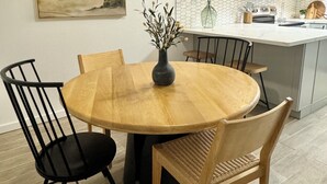 Un comedor con una mesa redonda de madera, cuatro sillas, un jarrón con flores y un ventilador de techo.