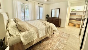 Un dormitorio con cama, cómoda, ventilador de techo y vista a un pasillo con estanterías.