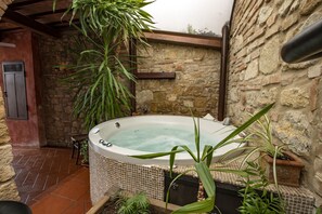 Ein Whirlpool in einem Außenbereich mit Steinwänden, Fliesenboden und Topfpflanzen.