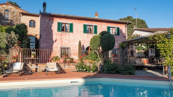 Ein Poolbereich mit Pool, Liegestühlen und einem Gebäude mit grünen Fensterläden.