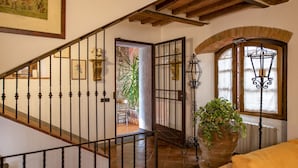 A staircase with a wrought iron railing, a potted plant, and a view into a room with a bed and a window. - Charming 4-bedroom villa in San Gimignano with private pool, hot tub and gym. (Toscana)