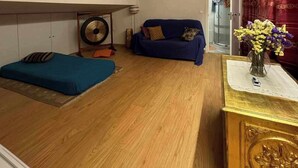 Une petite pièce accueillante, avec un canapé bleu, un lit, un plancher en bois et une petite table sur laquelle est posé un vase de fleurs.
