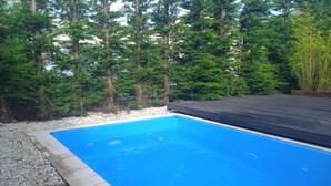 Une piscine rectangulaire aux parois bleues, bordée de galets et entourée d’une terrasse en bois.