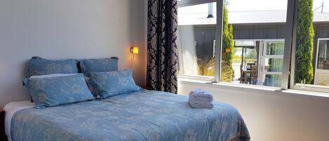 A bedroom with a bed, floral-patterned bedding, a window with curtains, and a view of the outside.