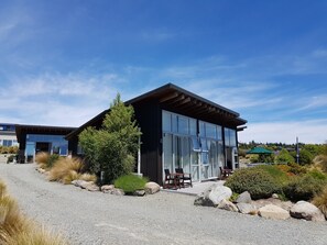 Un bâtiment moderne doté de grandes fenêtres en verre, d’une allée en gravier et d’une végétation luxuriante.