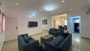 Una sala moderna con sofás oscuros, una mesa de centro y un televisor de pantalla plana montado en la pared.