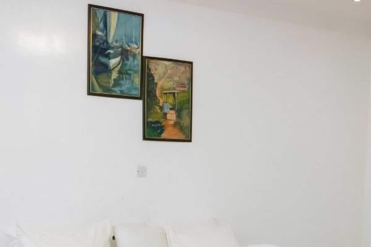 A bedroom with a large bed, white bedding, and two paintings on the wall.
