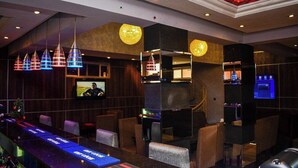 Zona de bar con una barra larga, varias lámparas colgantes y una pantalla de televisión.