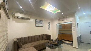 Una sala de estar moderna con sofá, mesa de centro y una pequeña cocina con armarios y refrigerador.