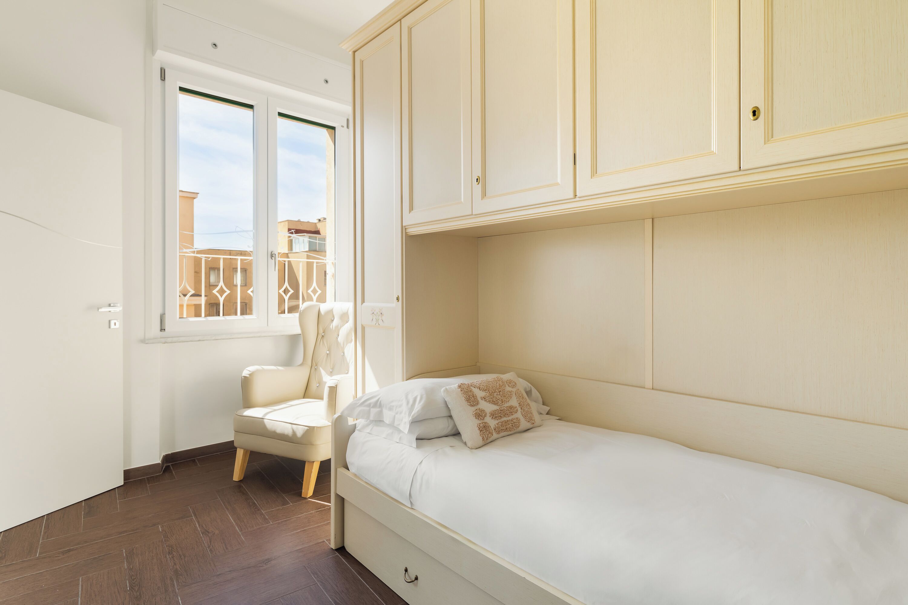 Un dormitorio pequeño y ordenado con una cama individual, una silla y un armario.
