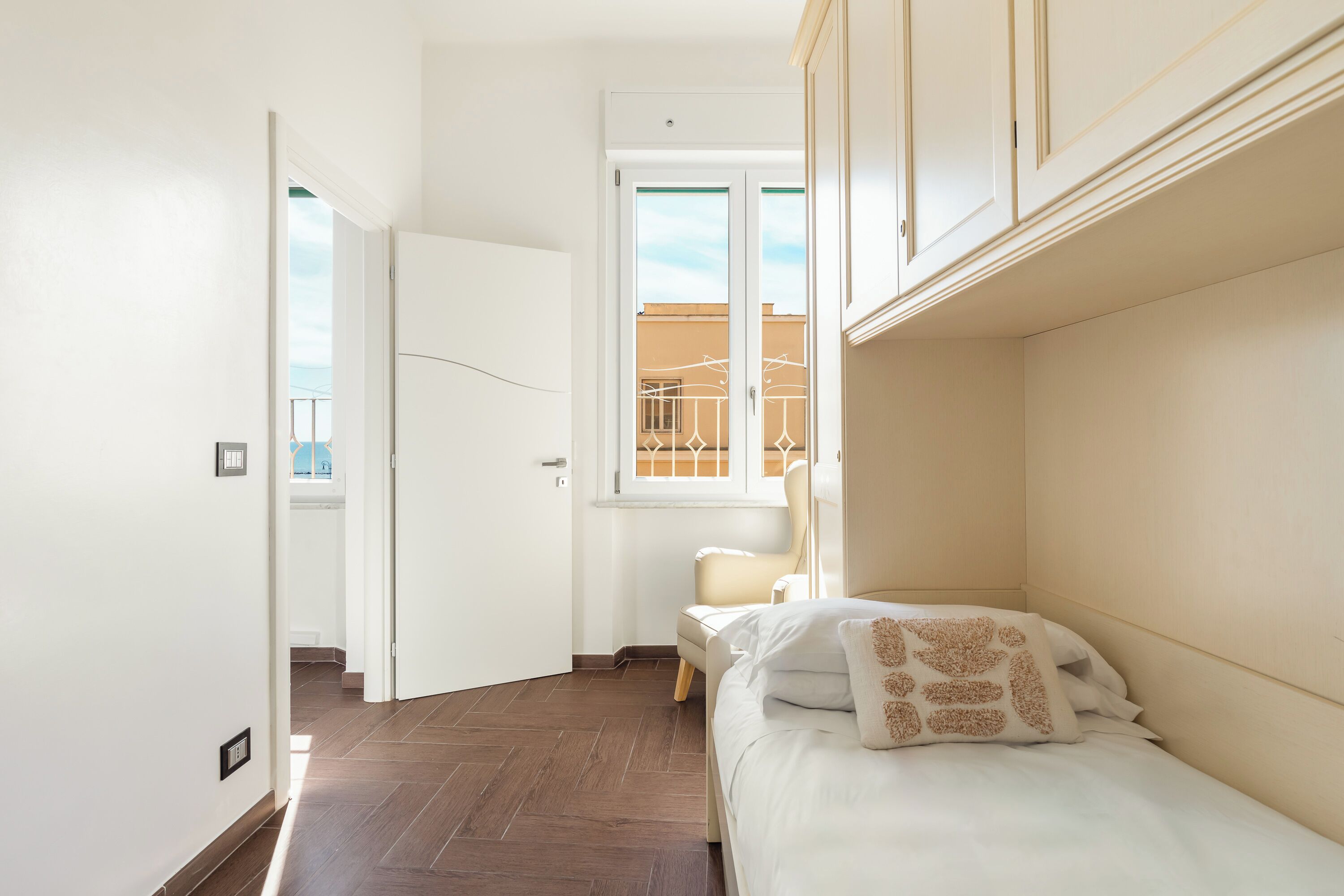 A bedroom with a bed, a chair, and a window with a view of buildings.