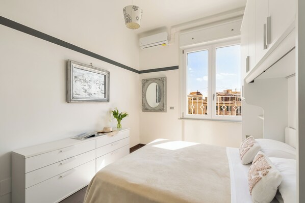 A modern bedroom with a bed, dresser, and large window. - Beach Apartment (Rome)