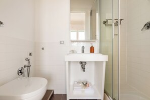 A modern bathroom with a white sink, a glass shower enclosure, and a white toilet. - Beach Apartment (Rome)