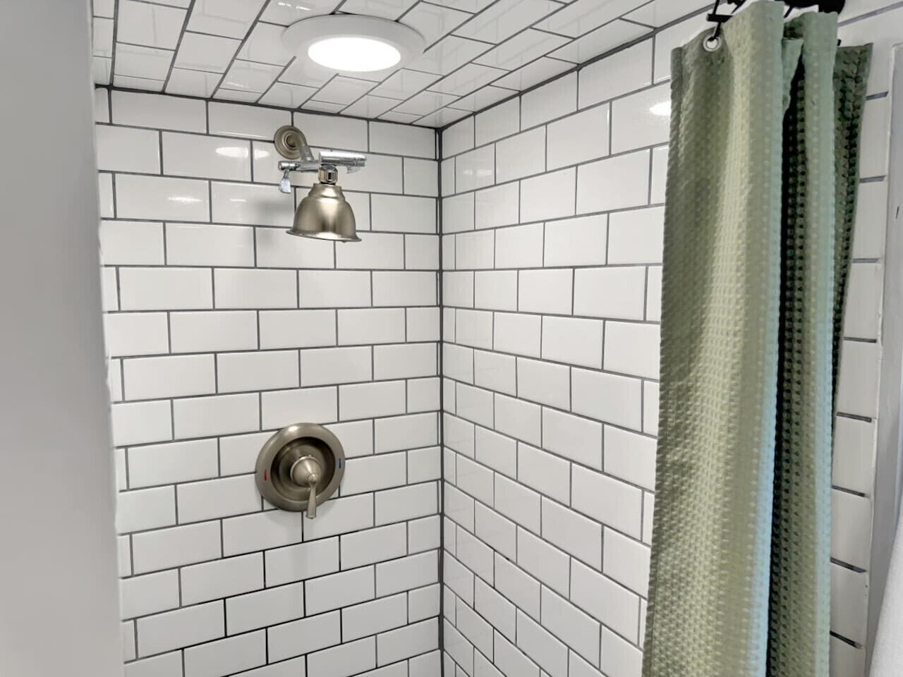 A corner shower with white subway tiles, a metallic showerhead, and a green shower curtain.