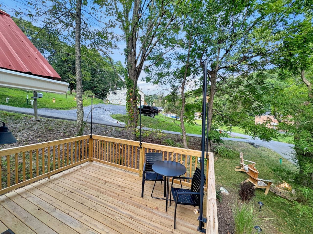 Una terraza de madera con una mesa y sillas, rodeada de árboles y una vista de la carretera.
