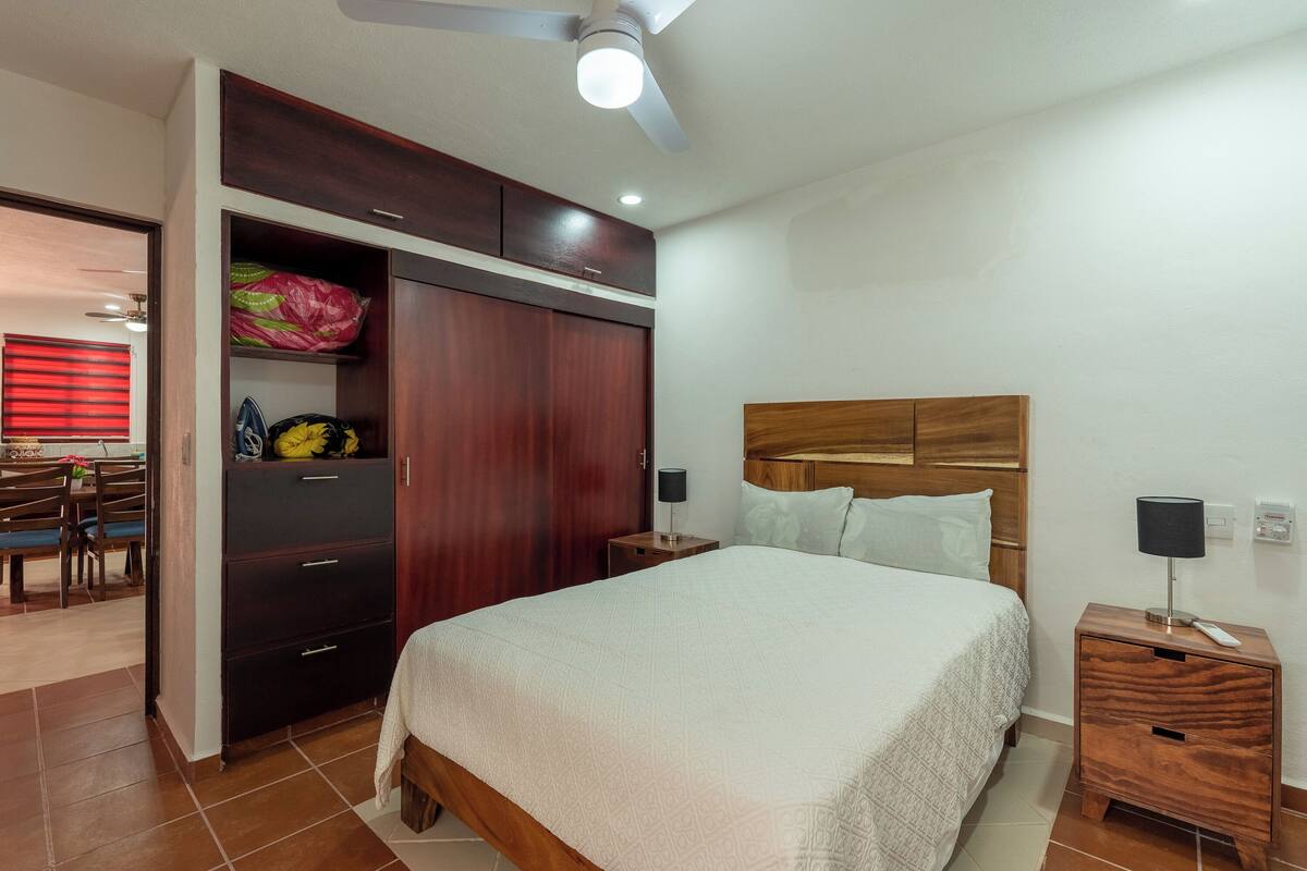 A bedroom with a bed, wooden headboard, nightstands, a wardrobe, and a ceiling fan.