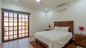 Une chambre à coucher comprenant un lit, des tables de chevet, un ventilateur de plafond, un appareil de climatisation et une porte-fenêtre coulissante.