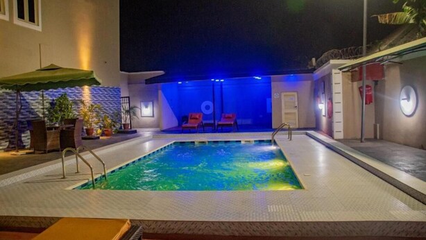 A swimming pool with a tiled deck, a small lounge area with chairs, and a covered seating area with umbrellas. - EdisPremier Hotel & Suites (Port Harcourt)