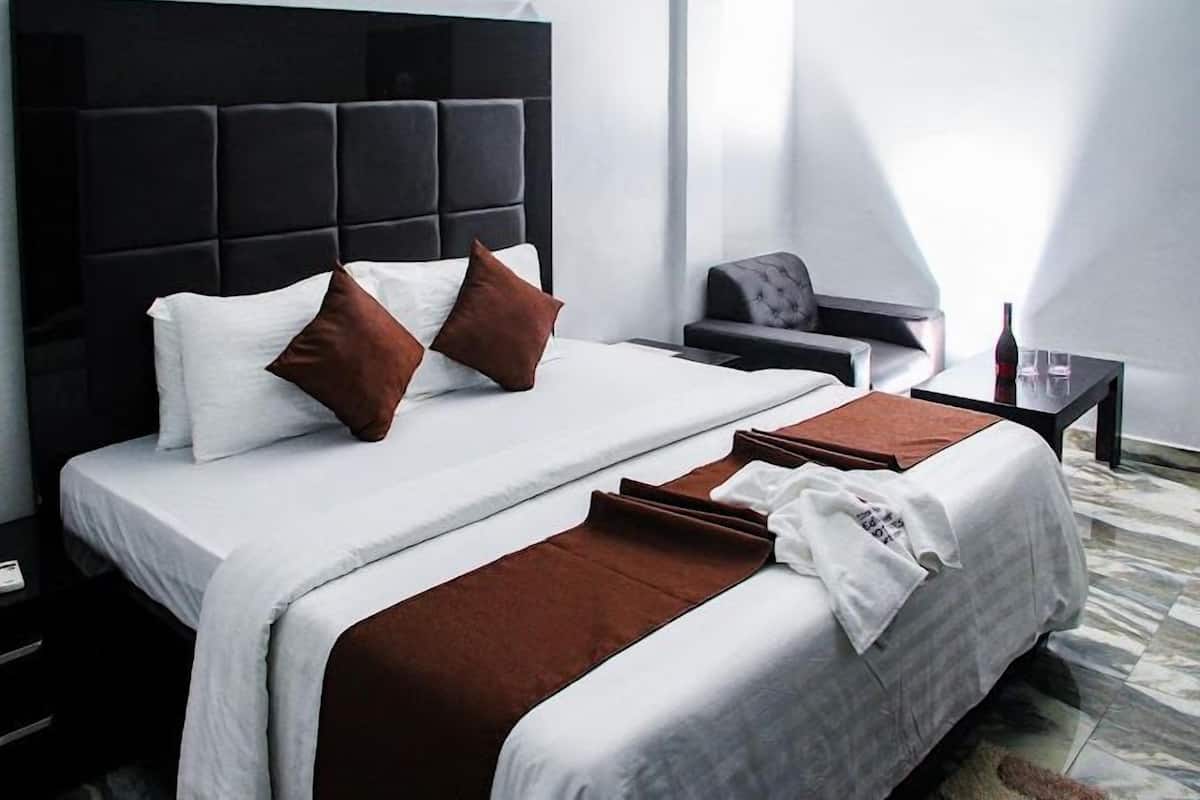 A modern hotel room with a large bed, a dark headboard, and a small seating area with a chair and a table.