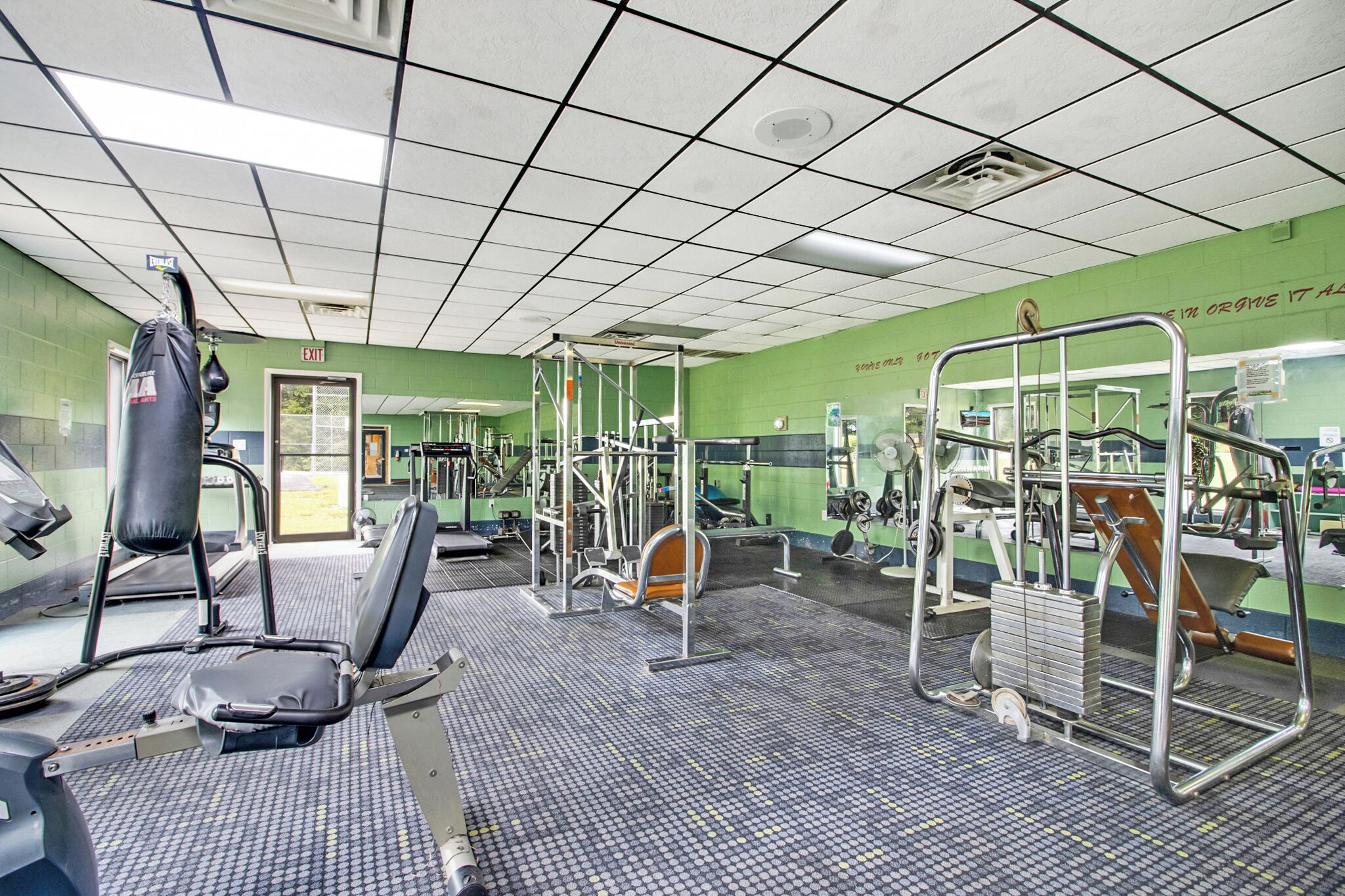 Un gimnasio con equipo de ejercicio, un saco de boxeo y un espejo grande.