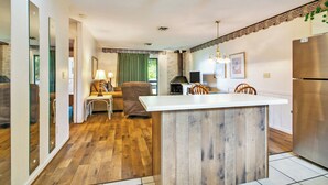 Una cocina moderna con una isla central, un comedor con cortina verde y una chimenea de ladrillo.