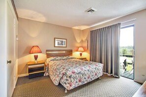 Habitación de hotel con cama, dos lámparas de noche, un cuadro en la pared y vistas al exterior a través de una puerta corredera.