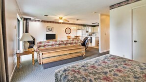Habitación de hotel con cama, escritorio con lámpara, televisor, kitchenette y ventilador de techo.