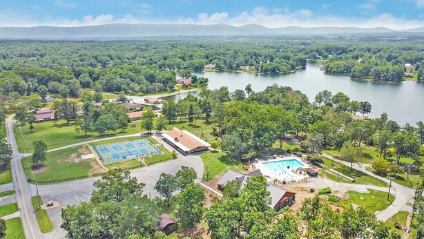 Vista aérea de una zona residencial con una piscina grande, canchas de tenis y un lago al fondo.
