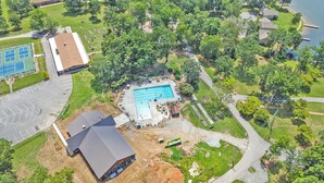 Vue aérienne d’un quartier résidentiel avec une piscine, des courts de tennis et un grand bâtiment doté d’un toit en pente.