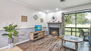 Un salon avec une cheminée, un téléviseur et une grande fenêtre donnant sur un jardin.