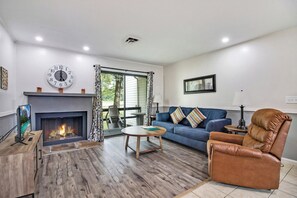 Una sala de estar con chimenea, un sofá, un sillón de cuero, una mesa de centro y un televisor sobre un mueble.