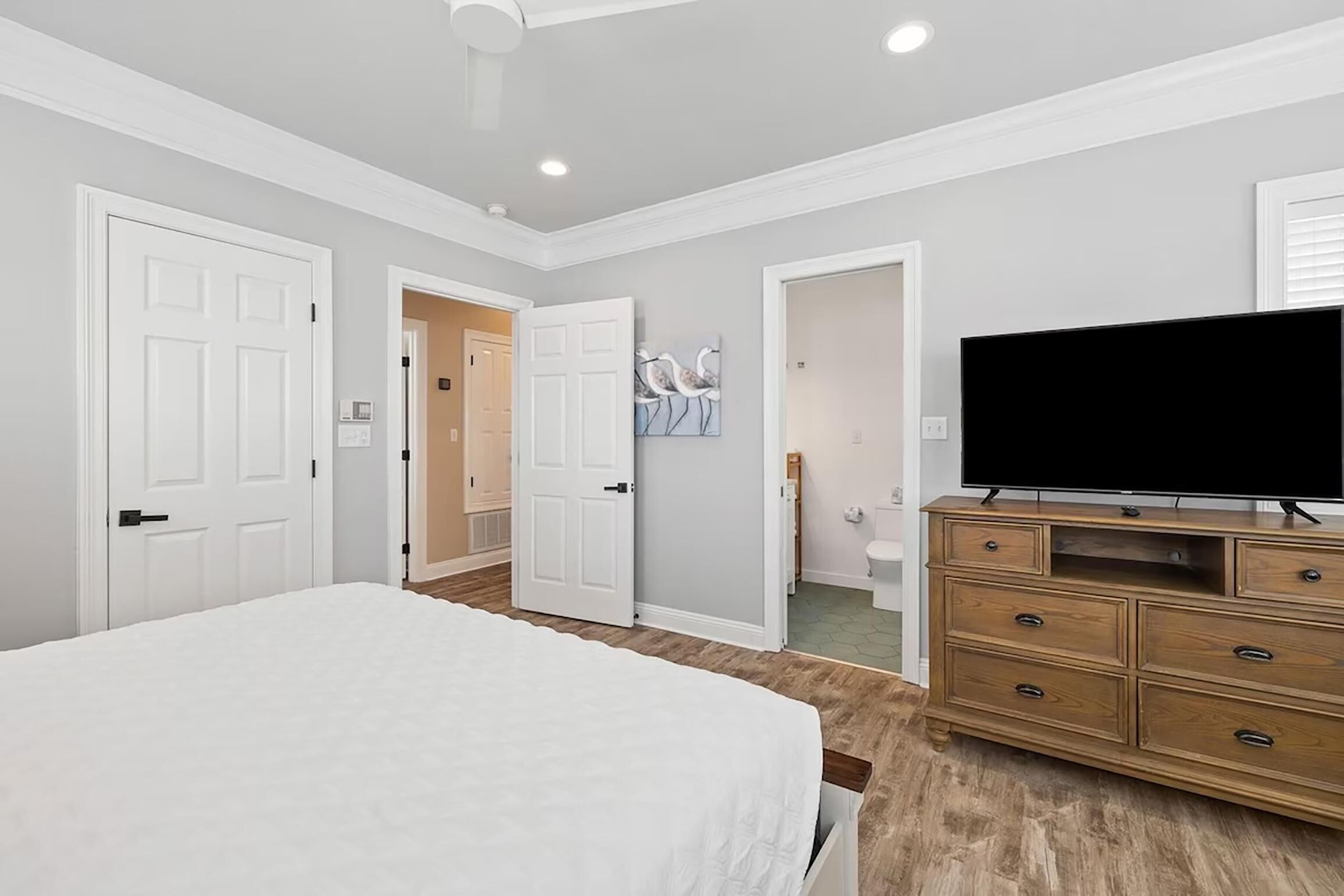 A bedroom with a bed, a dresser, a television, and two doors leading to other rooms.