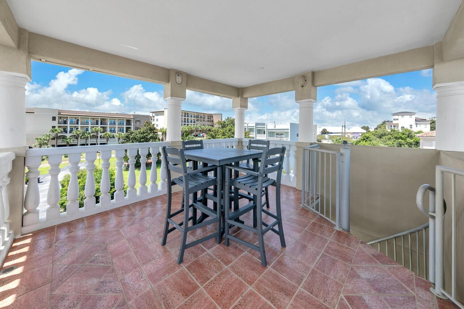 Ein überdachter Balkon mit Tisch und Stühlen, weiße Geländer und Blick auf umliegende Gebäude.