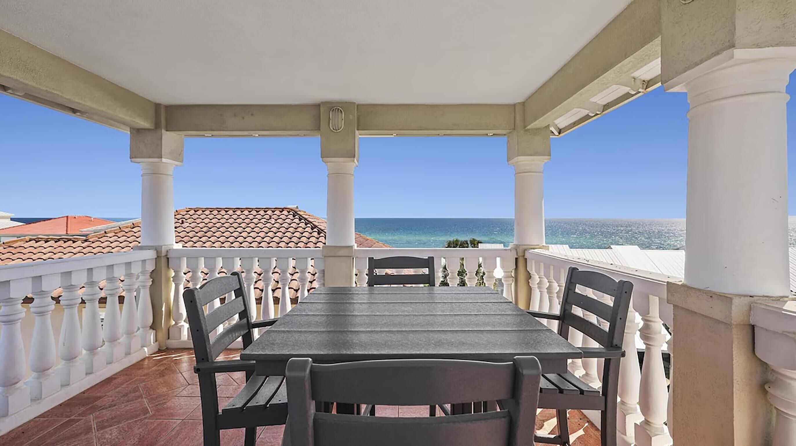A covered balcony with a table and chairs, overlooking the sea.