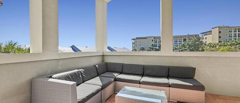 A covered outdoor seating area with a large sectional sofa and a small table, overlooking a residential area.