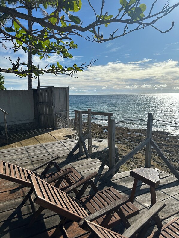 A wooden deck with lounge chairs overlooking a beach.