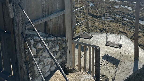 Une structure en bois, dotée d’une rambarde métallique, surplombe une plage rocheuse et l’océan.