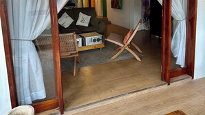 Une pièce avec un plancher en bois, un canapé, une petite table et un banc. Il y a une porte avec des rideaux.
