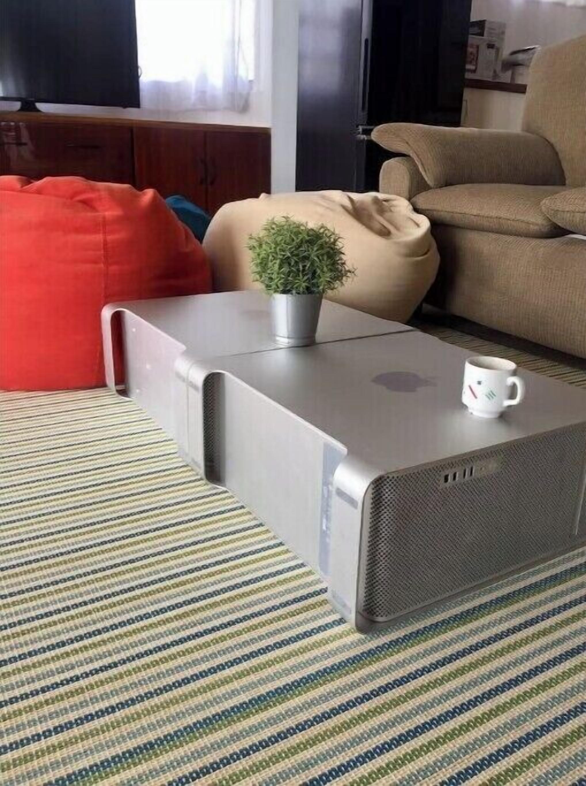 A modern living room with a grey entertainment unit, a small potted plant, a white mug, and a red bean bag.