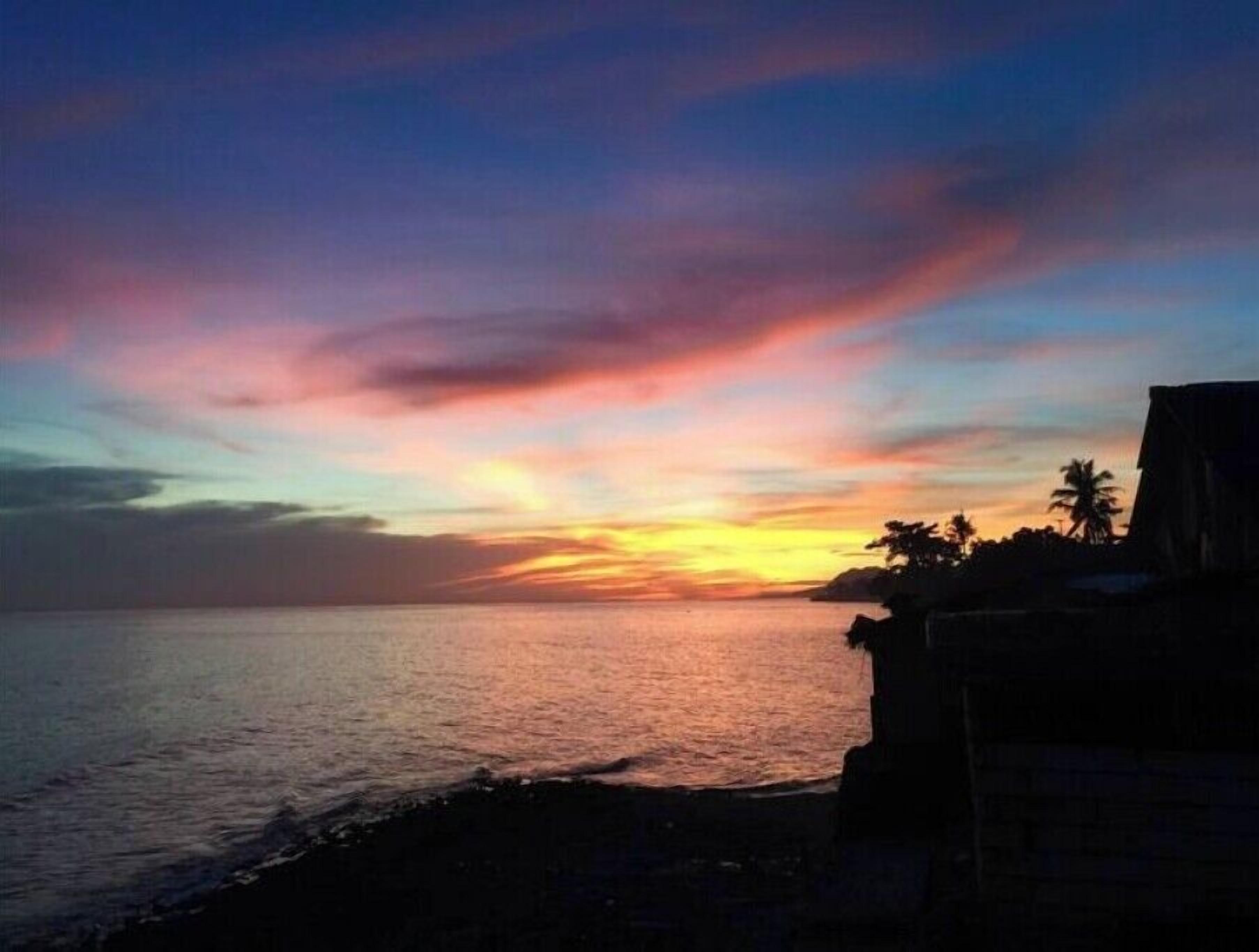 A sunset over a calm sea with a silhouette of a building on the right.