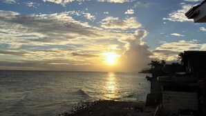 Une plage où le soleil se couche à l’horizon, sous un ciel dégagé, et où la mer est calme.