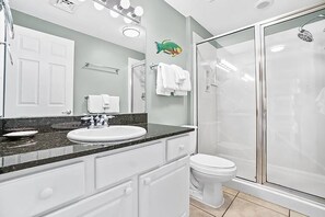 Une salle de bain avec un lavabo blanc, un miroir et des toilettes. On y trouve une douche avec une porte en verre et un porte-serviettes avec des serviettes blanches.