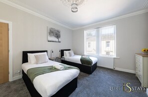 Ein Hotelzimmer mit zwei Betten, einem Heizkörper, einem Fenster mit Jalousien und einem kleinen Tisch mit Lampe.
