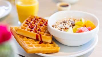 A breakfast setting with waffles, a bowl of fruit and granola, and a glass of orange juice.