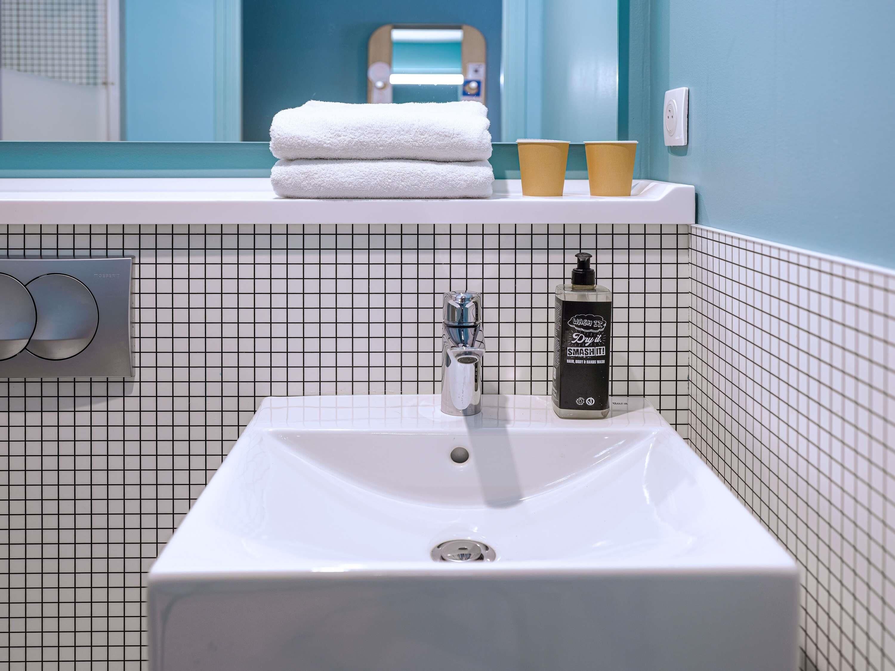 A bathroom with a white sink, a mirror, a towel stack, and a bottle of hand soap.